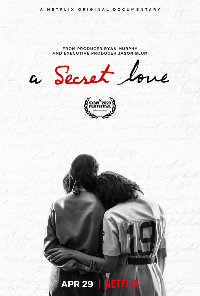 Poster for A Secret Love, featuring a black-and-white image of two women with their backs to the camera. The woman on the right, who is wearing a 1940s-style baseball uniform, rests her head on the other woman's shoulder, and the two women hold each other's arms affectionately behind their backs.